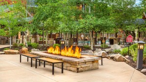 An outdoor patio with a stone fire feature, seating, and a pool area in the background. - Hilton Grand Vacations Club Sunrise Lodge Park City (Park City)