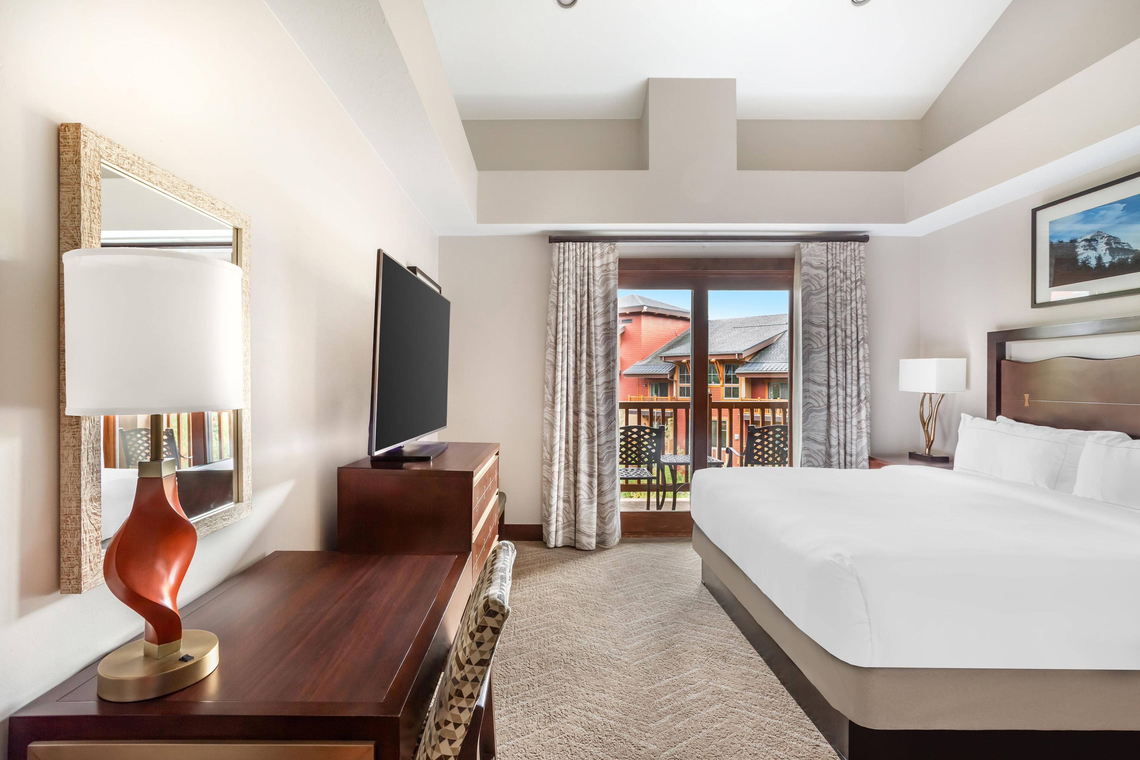 Ein Hotelzimmer mit Bett, Fernseher, Schreibtisch, Stuhl, Lampe und Blick ins Freie.