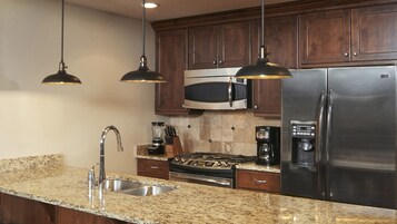 A kitchen with granite countertops, stainless steel appliances, wooden cabinets, and pendant lighting.