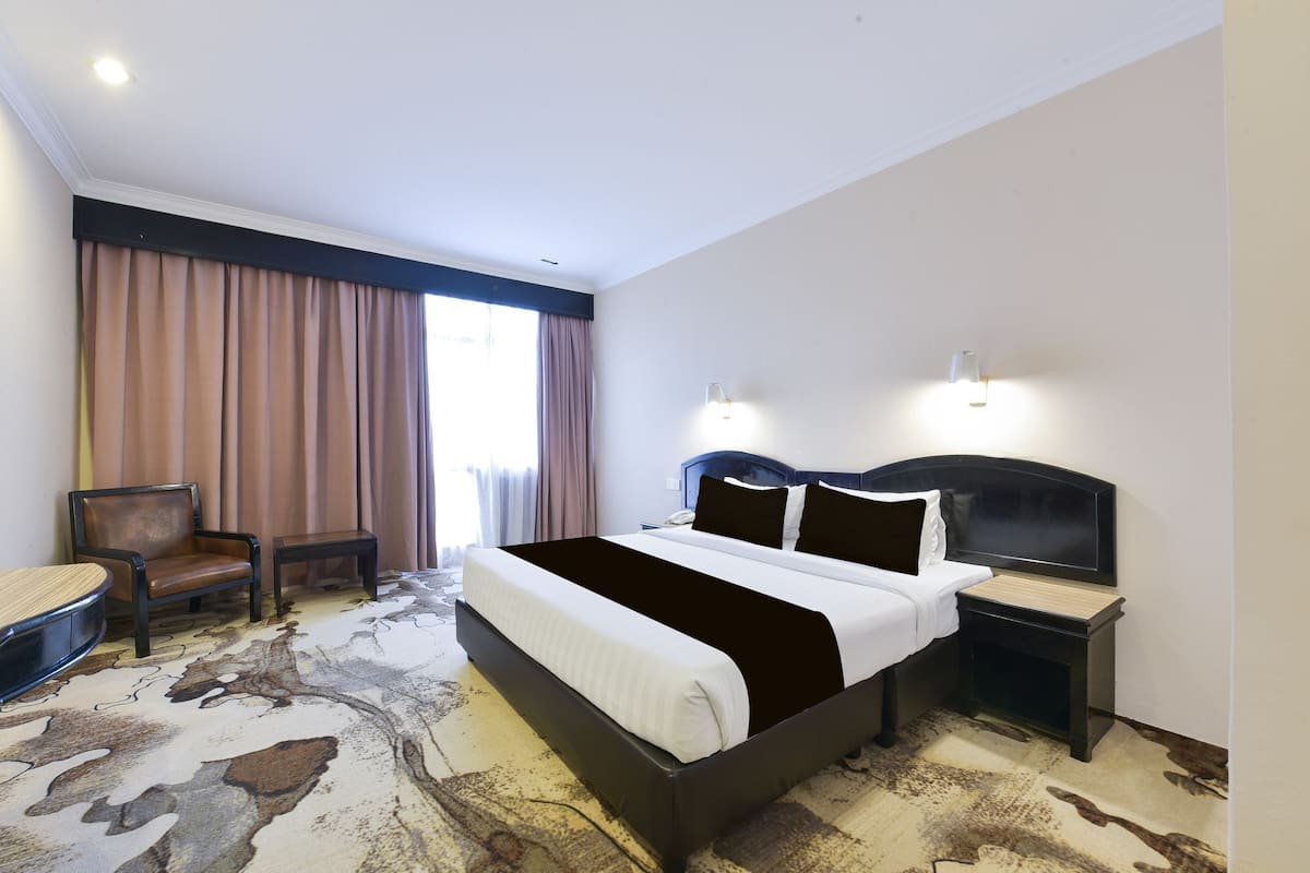 A hotel room with a large bed, a desk, a chair, and a window with curtains.
