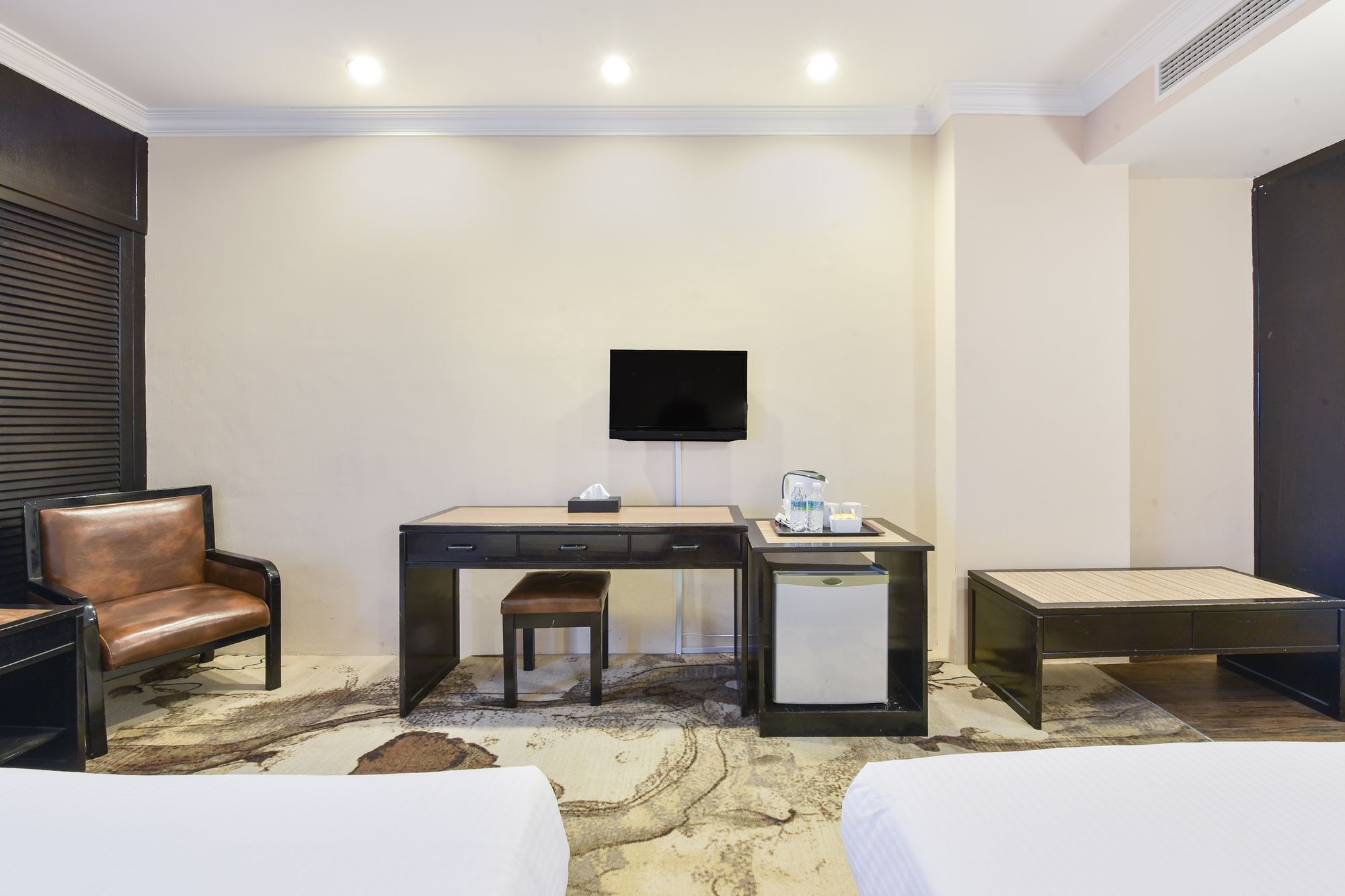 A hotel room with a desk, chair, TV, and two beds.