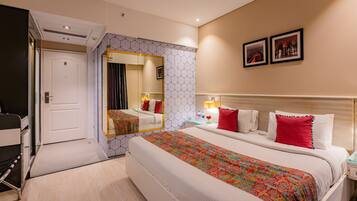 A hotel room with a large bed, a bedside table with a lamp, a mirror, and two framed pictures on the wall.