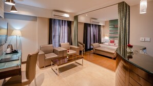 A modern hotel room with a glass desk, two sofas, a bed, and a large mirror. - Regenta Inn Jaipur (Jaipur)