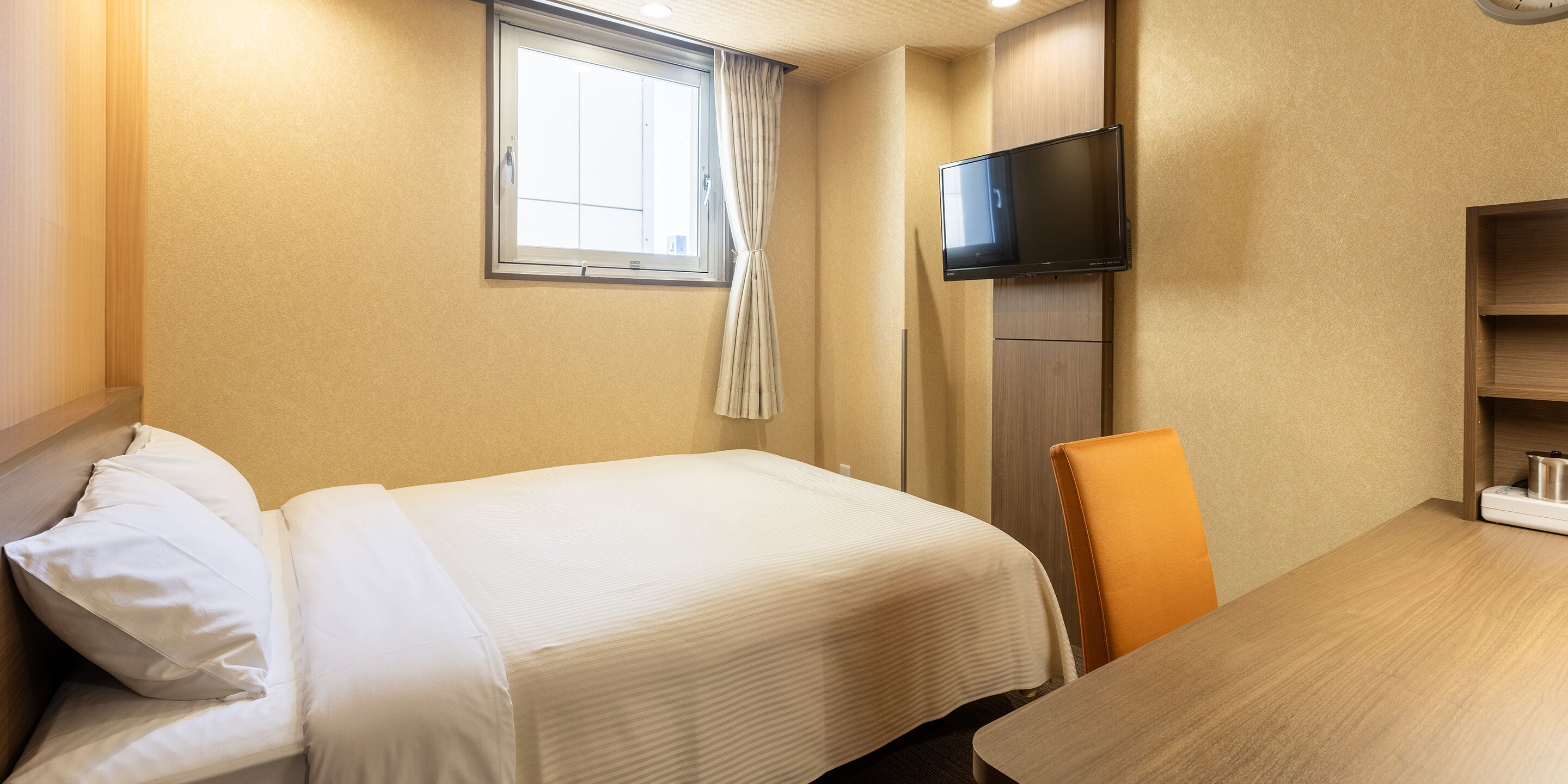 Habitaci ón de hotel con cama, televisión montada en la pared, ventana con cortinas y una mesa de madera.