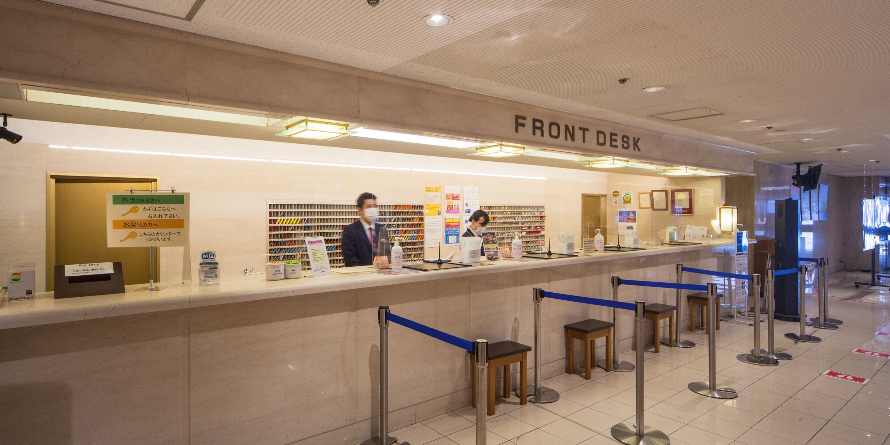 A front desk area with a sign reading "FRONT DESK," a counter with various items, and a queue of people waiting.