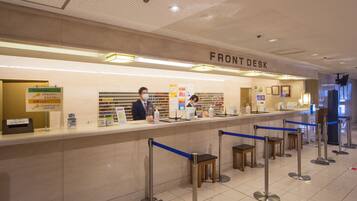 A front desk area with a sign reading "FRONT DESK," a counter with various items, and a queue of people waiting.