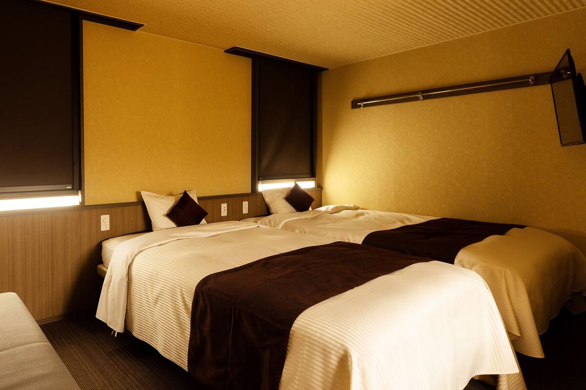 Una habitación de hotel con dos camas, un sofá y una ventana con persianas.