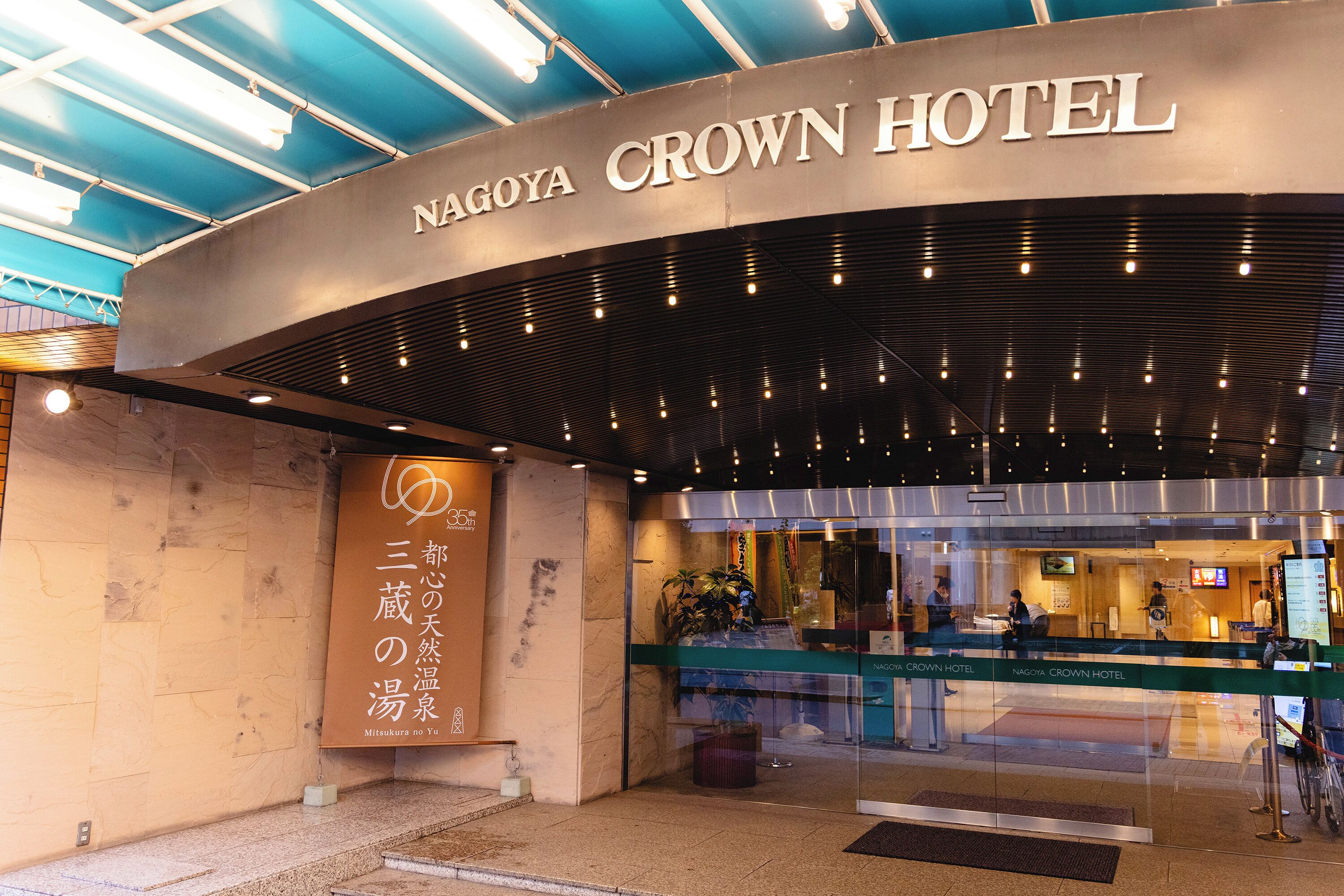 The exterior of Nagoya Crown Hotel with a modern design, a reception area visible through glass doors, and signage in both English and Japanese.