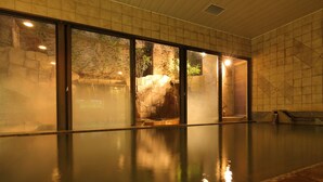 A spacious indoor pool area with clear glass walls, a stone wall, and a tiled floor. - Nagoya Crown Hotel (Nagoya)