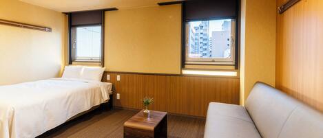 Una habitación de hotel con dos camas, una mesita de madera y vistas a la ciudad a través de dos ventanas.