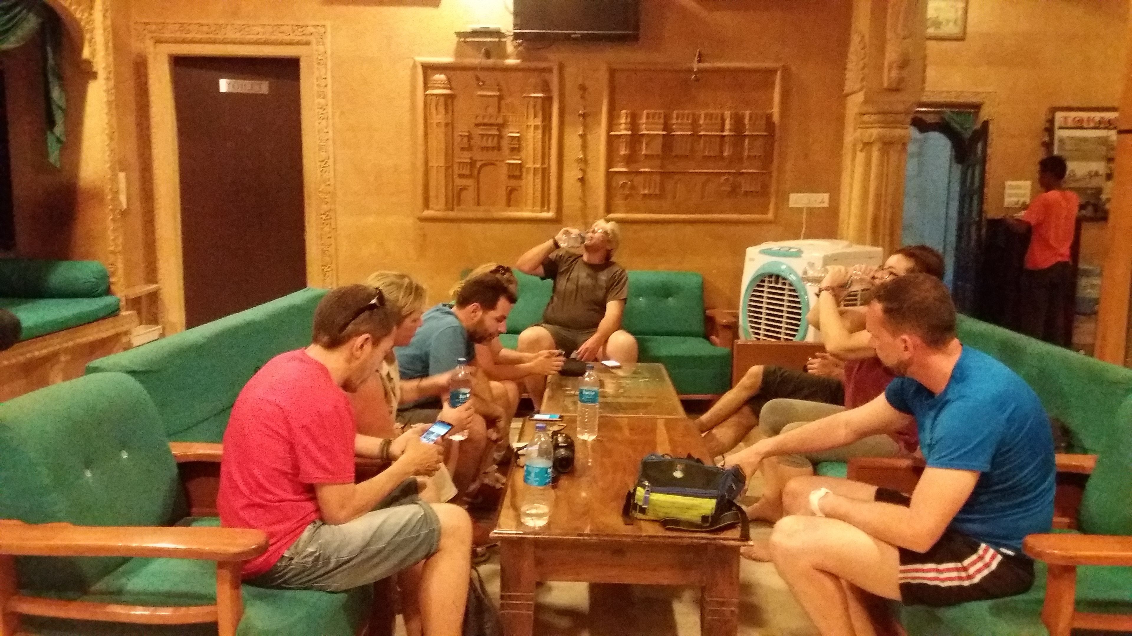 A group of people seated around a wooden table in a room with green upholstered chairs and a wooden floor.
