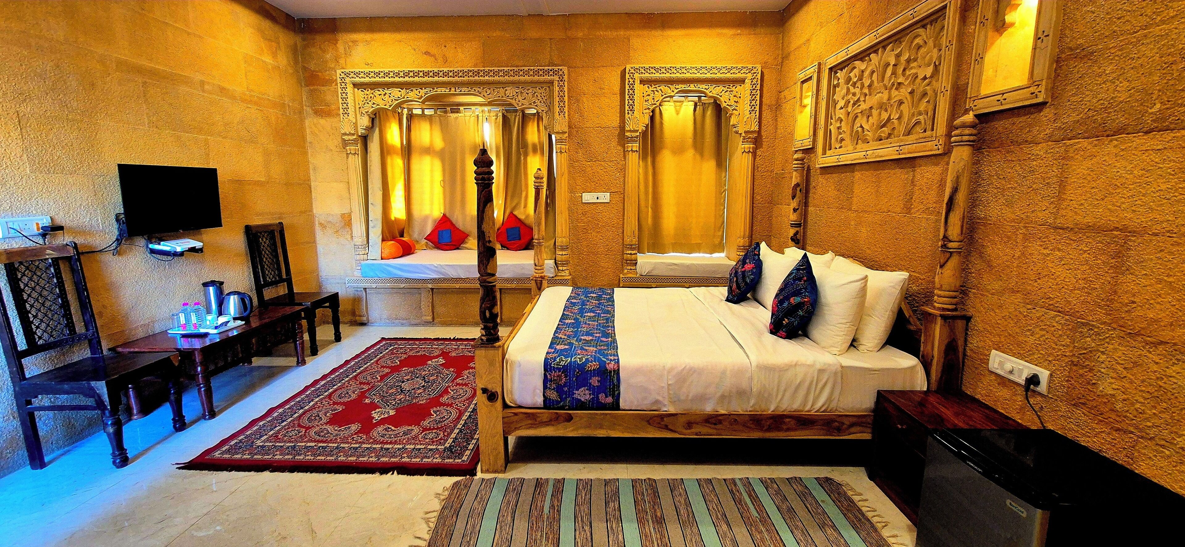 A hotel room with a large bed, a television, a desk, and a red and blue patterned rug.