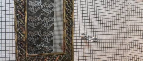 Un baño con un lavamanos negro, un espejo con marco decorativo y una pared de azulejos.