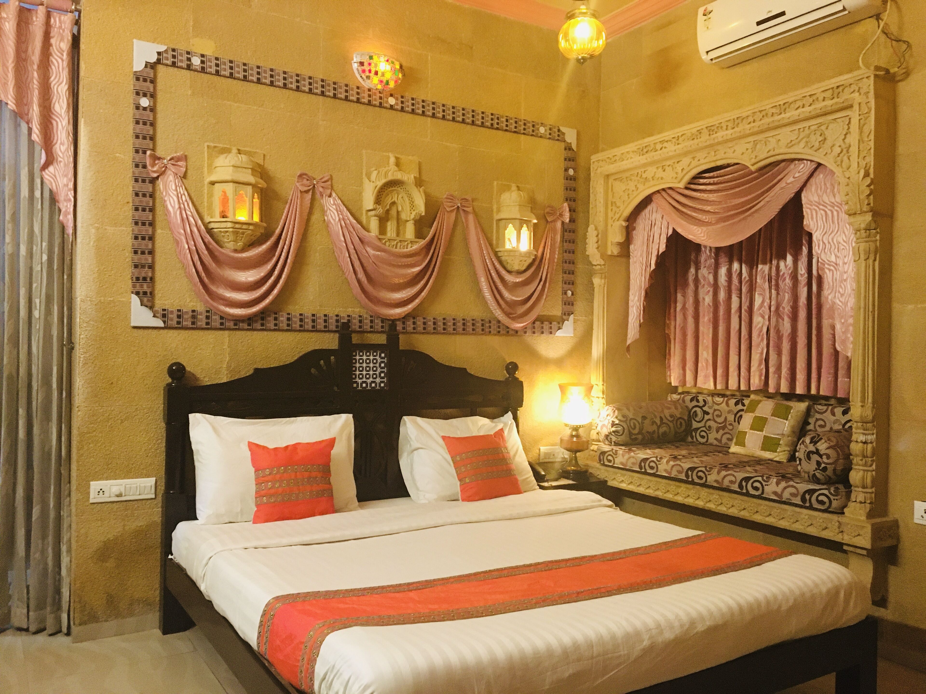Une chambre d’hôtel dotée d’un grand lit, d’un canapé, d’appliques murales décoratives et d’une cheminée ornée.
