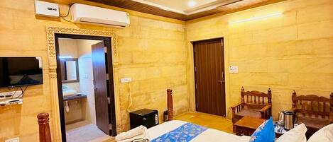 Quarto de hotel com cama, ventilador de teto, ar condicionado, televisão e porta de madeira.