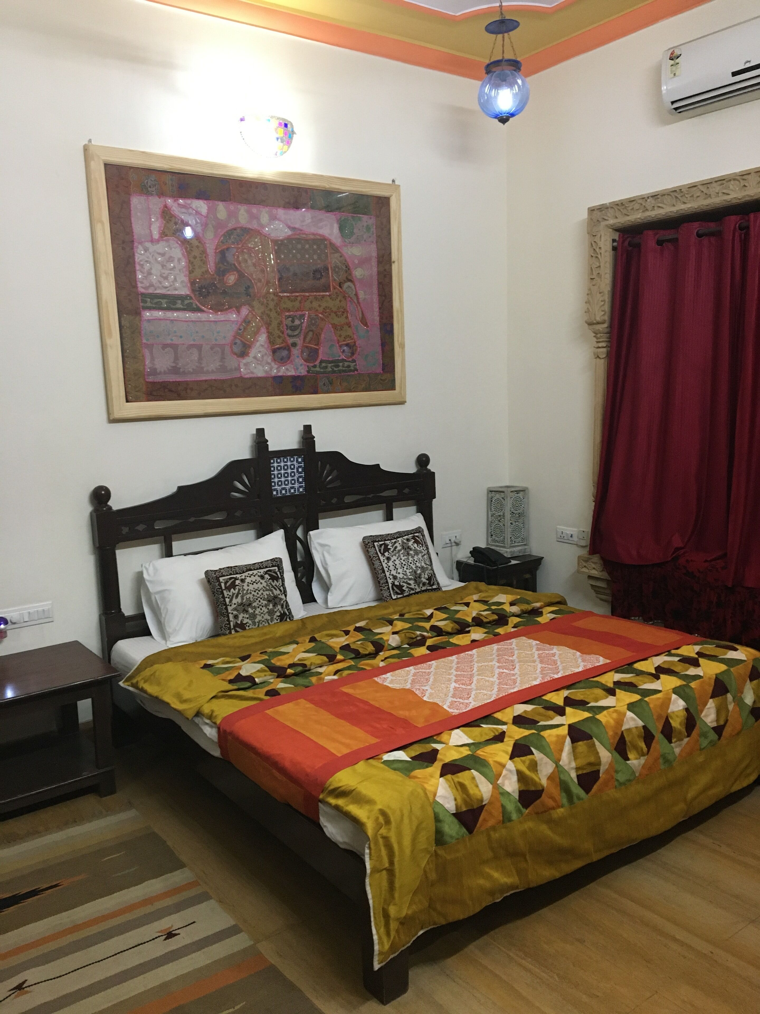 A bedroom with a bed, a nightstand, a wall-mounted air conditioner, a decorative light fixture, and a framed picture on the wall.