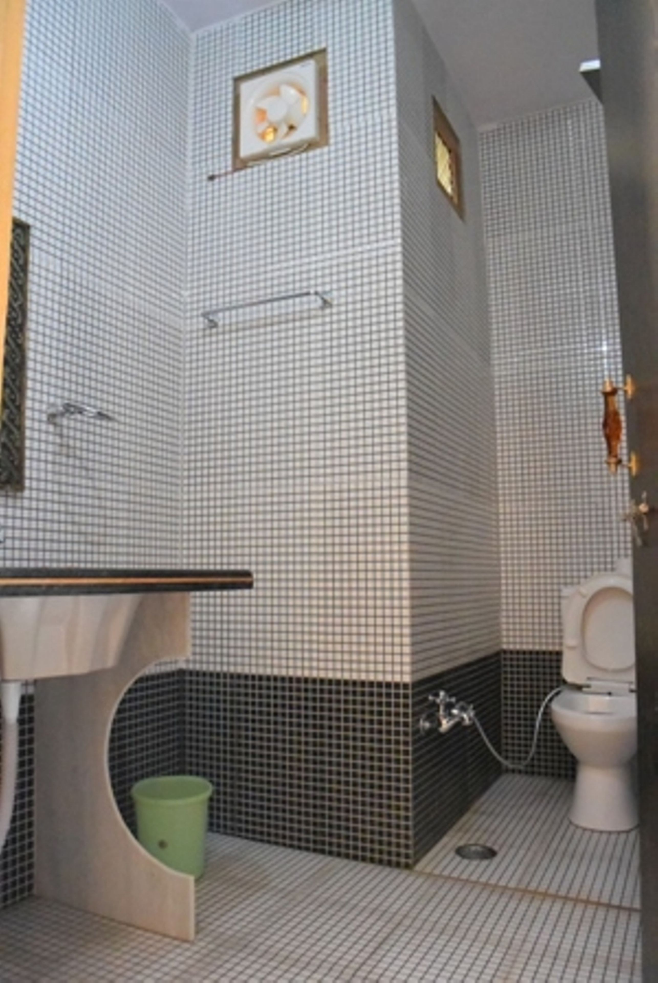 A bathroom with a checkered tile pattern, a toilet, a sink with a mirror, and a green trash bin.