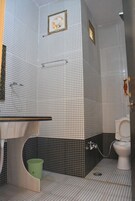 Un baño con piso de baldosas a cuadros, un inodoro, un lavabo con espejo y un bote de basura verde.