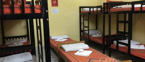 A dormitory room with bunk beds, a bed, a small table, and a wall clock.