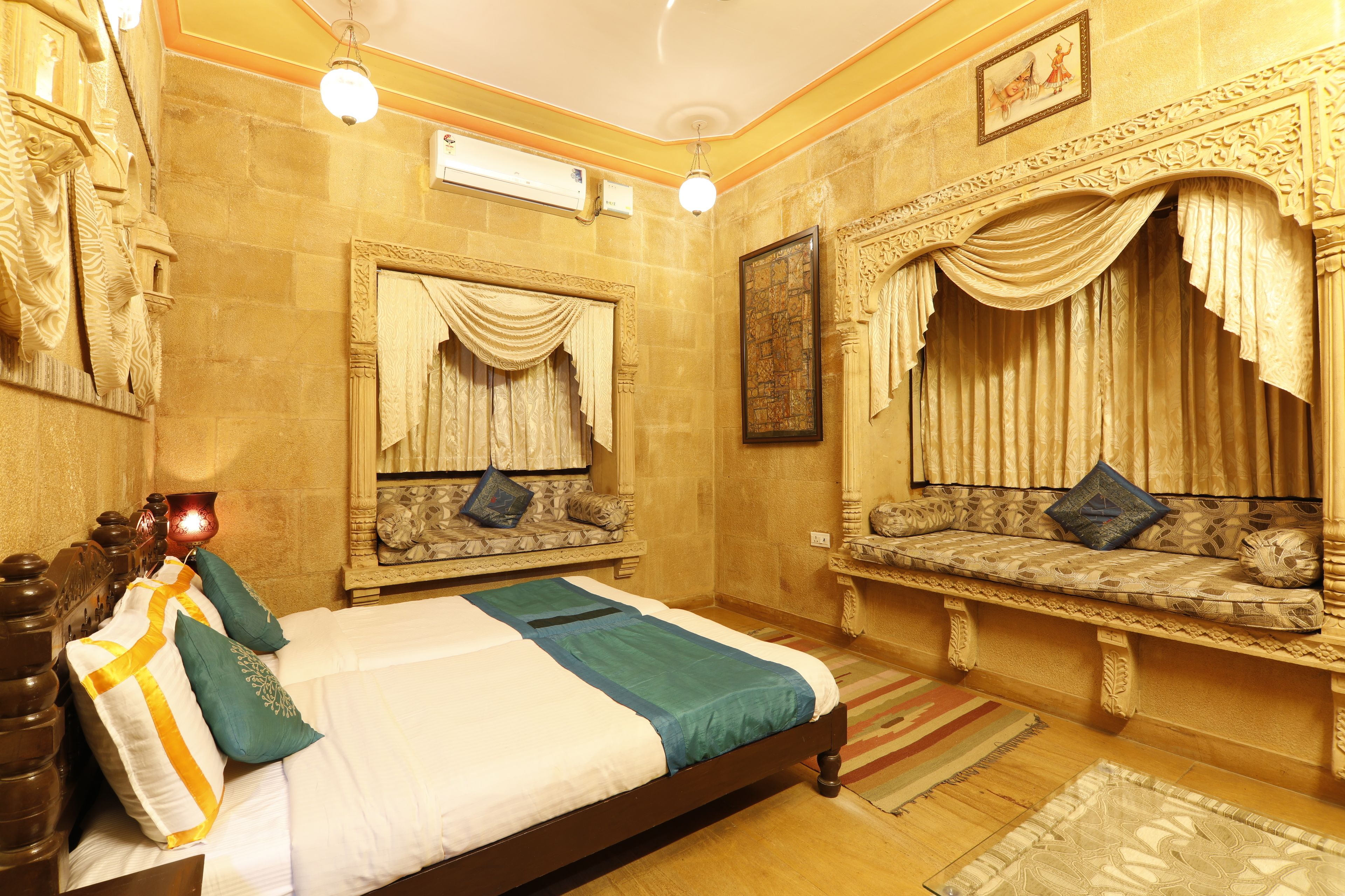 Une chambre d’hôtel avec un grand lit, une banquette avec des coussins, un miroir décoratif et une œuvre d’art encadrée au mur.