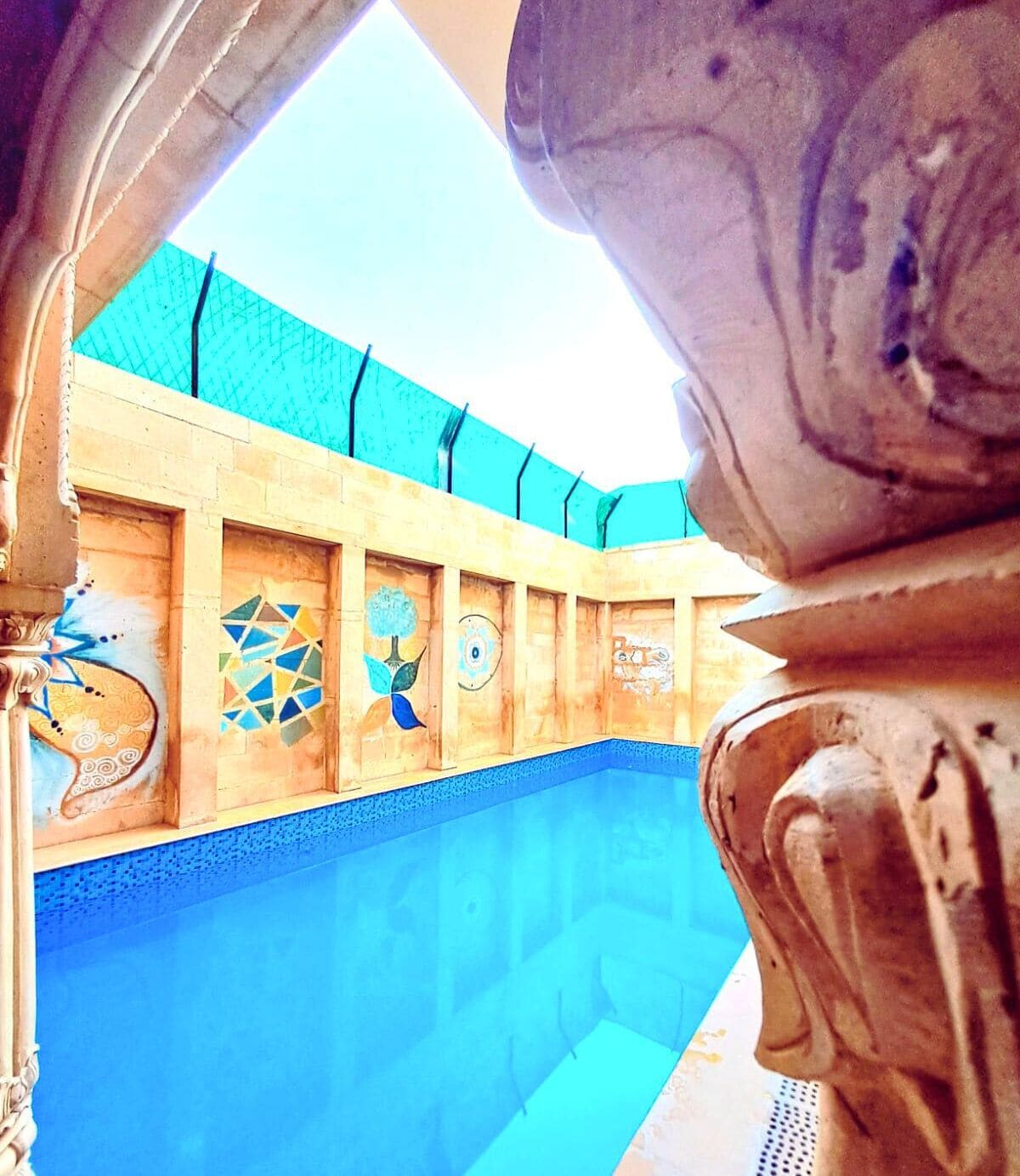 Una piscina con terraza de madera y mosaicos.