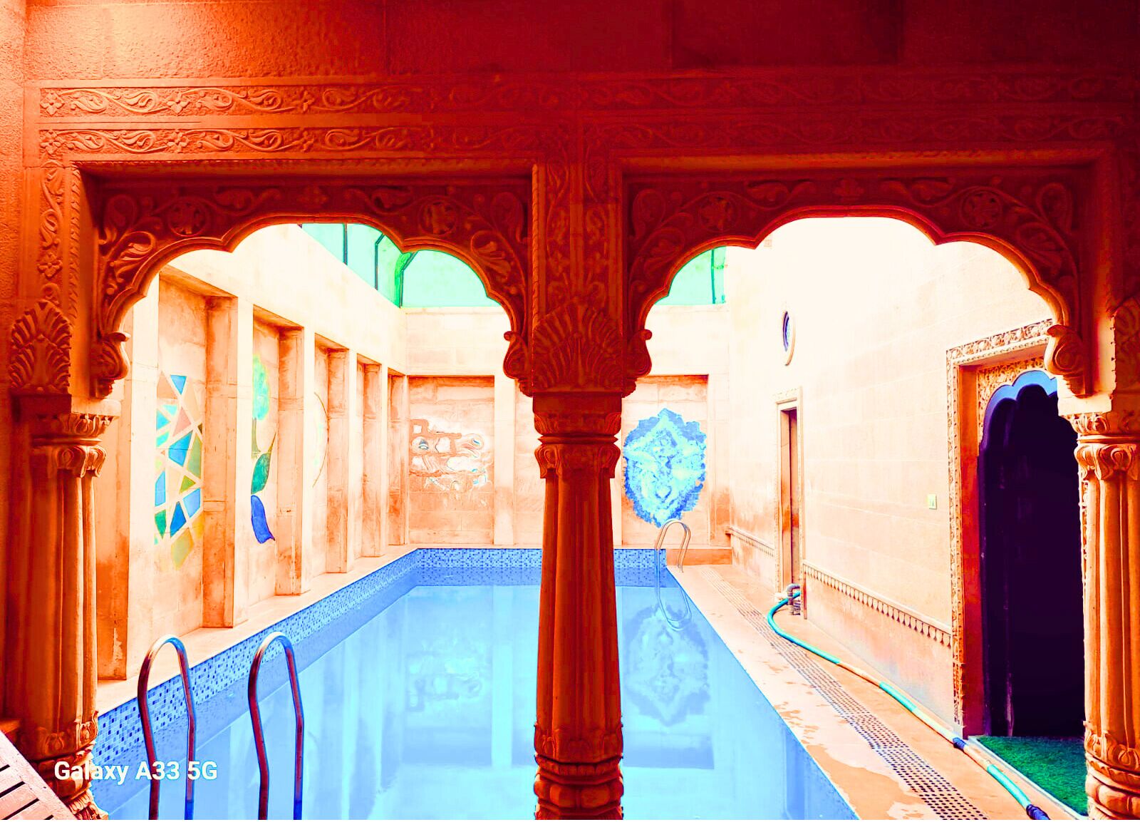 Un espace piscine intérieur agrémenté d’arches et de colonnes décoratives, d’un sol carrelé et offrant une vue à travers les arches.