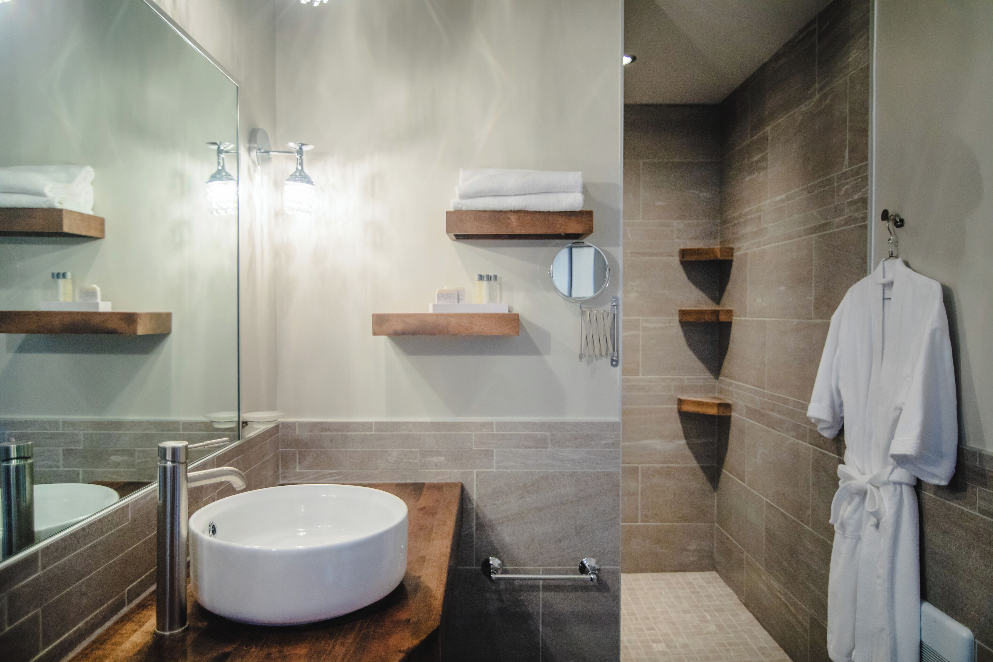 Un baño moderno con un lavamanos redondo, estantes de madera, una bata colgada y un espejo.