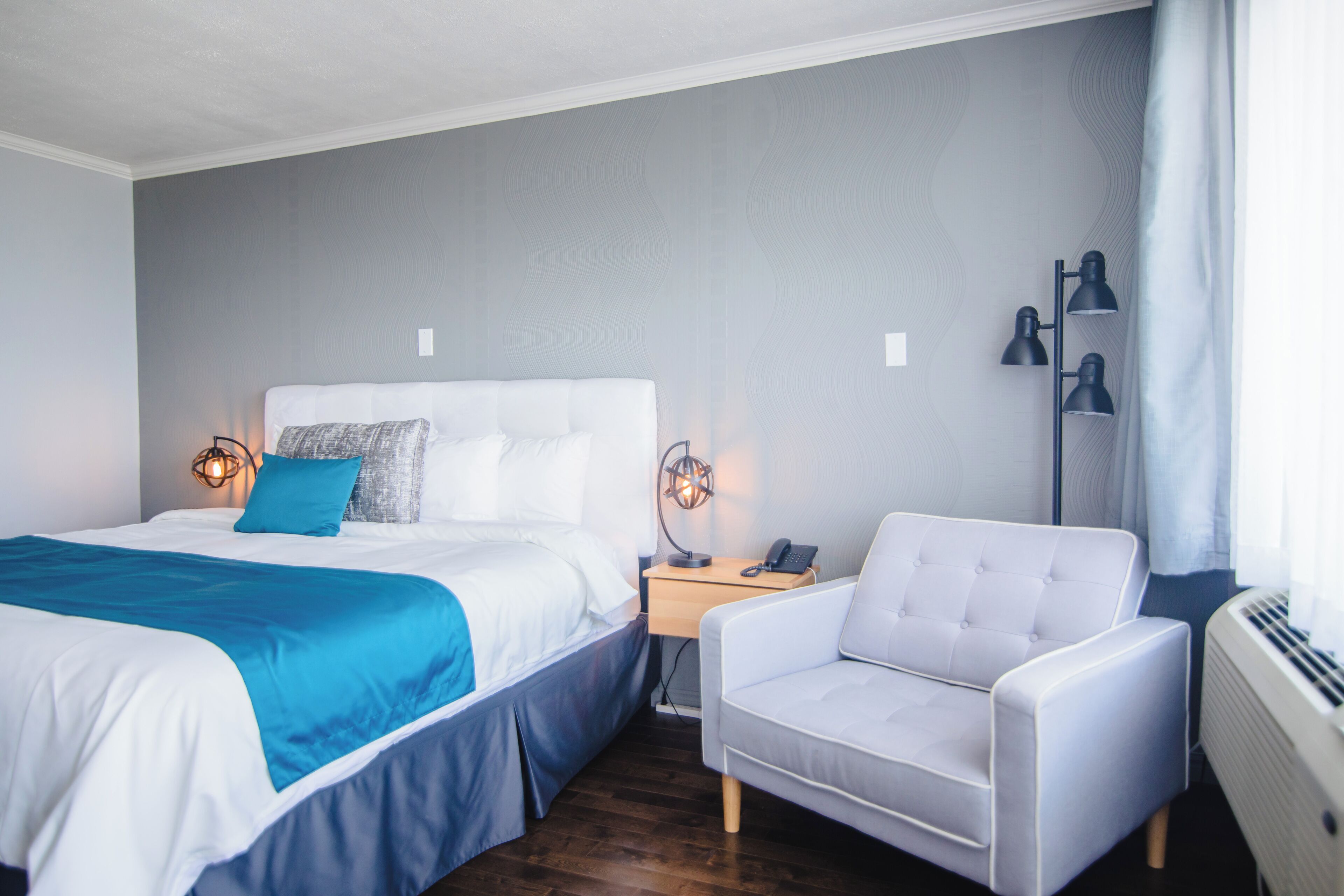Een hotelkamer met een groot bed, een nachtkastje met een lamp, een stoel en een radiator.