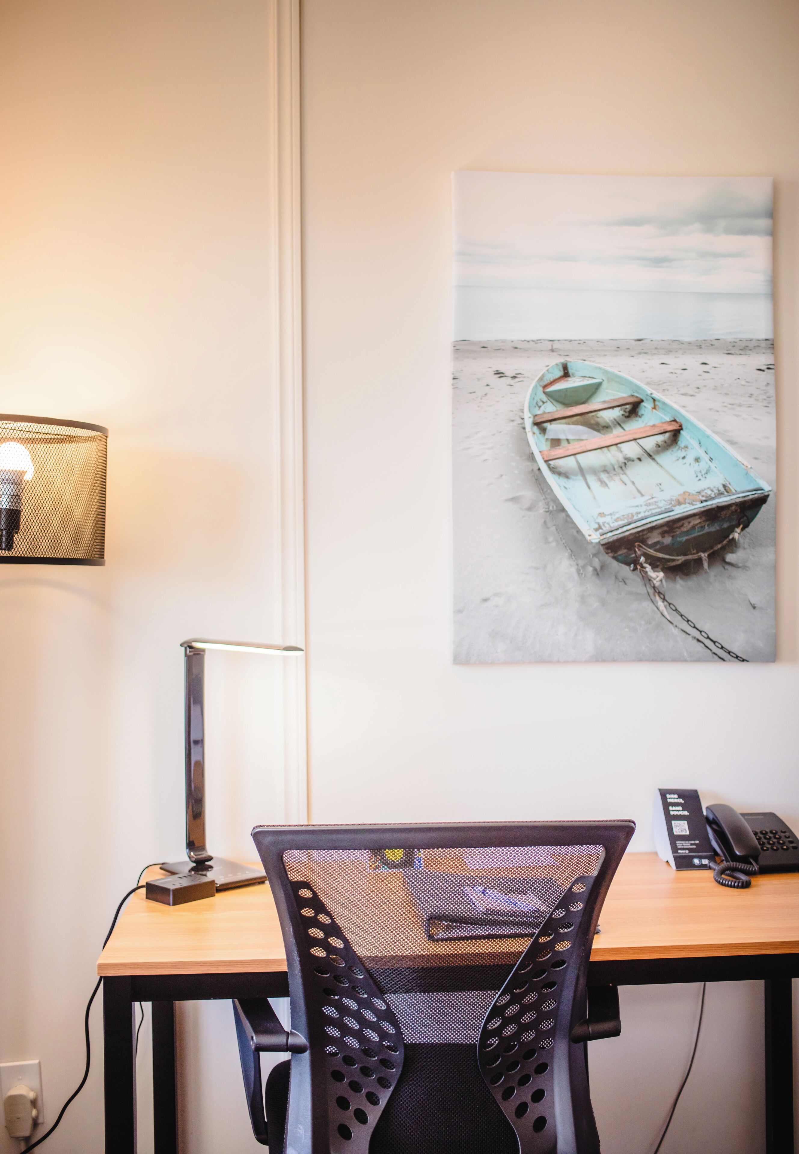 Un bureau avec une chaise, une lampe, un téléphone et un tableau représentant un bateau sur une plage.