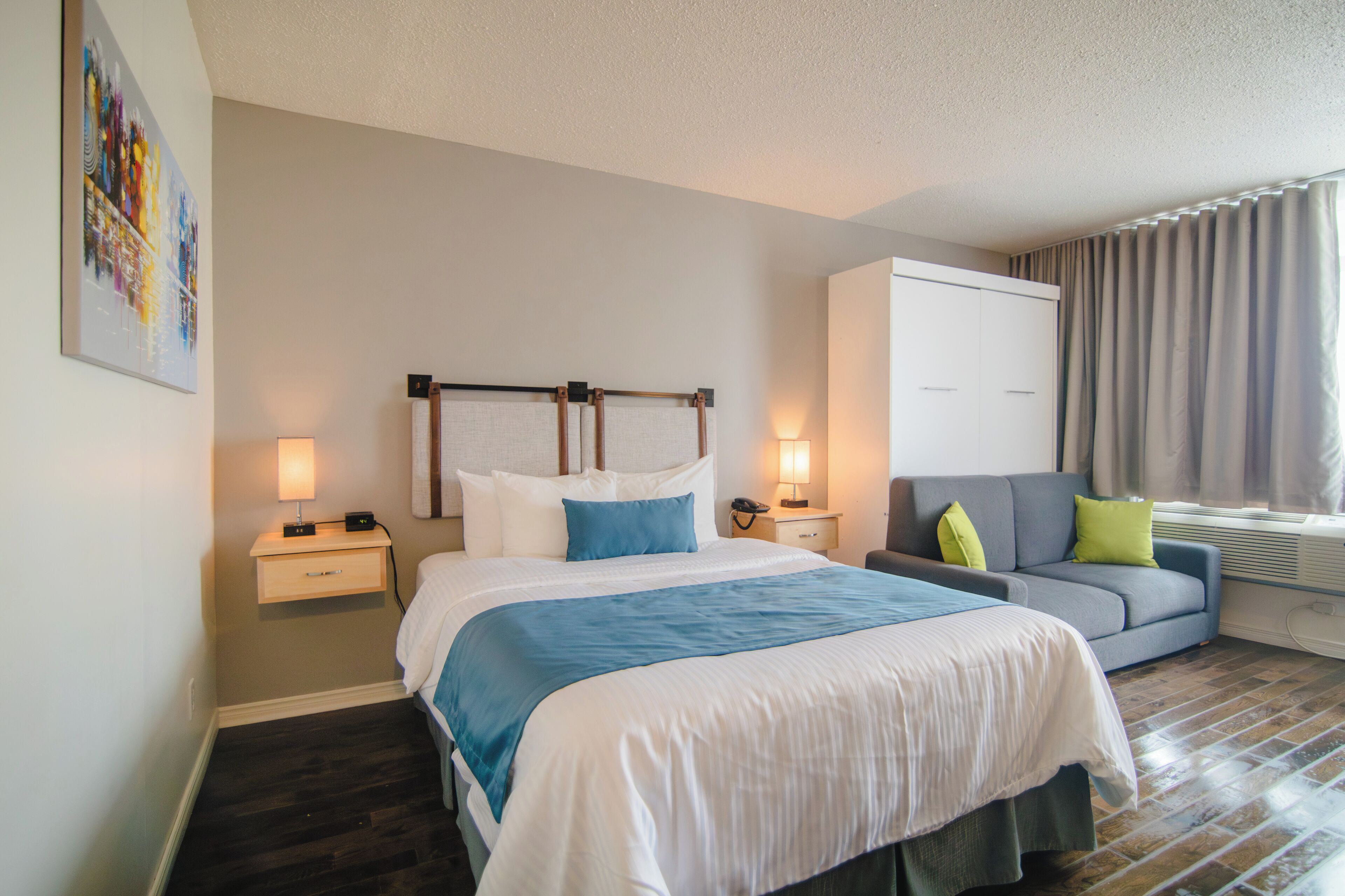 A hotel room with a large bed, a sofa, a desk, and a window with curtains.