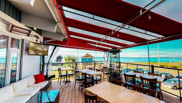 Een overdekt terras met tafels en stoelen, met uitzicht op een waterpartij.
