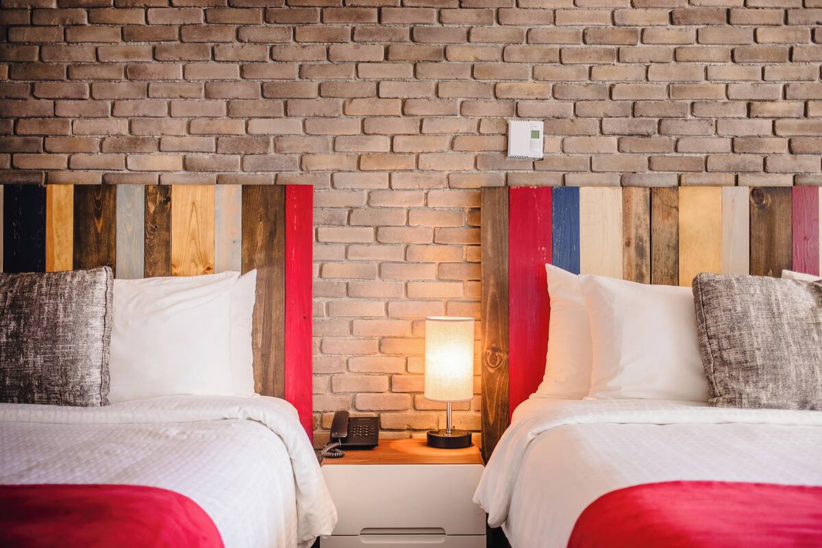 Una habitación de hotel con dos camas, un muro de ladrillo y un cabecero de madera.