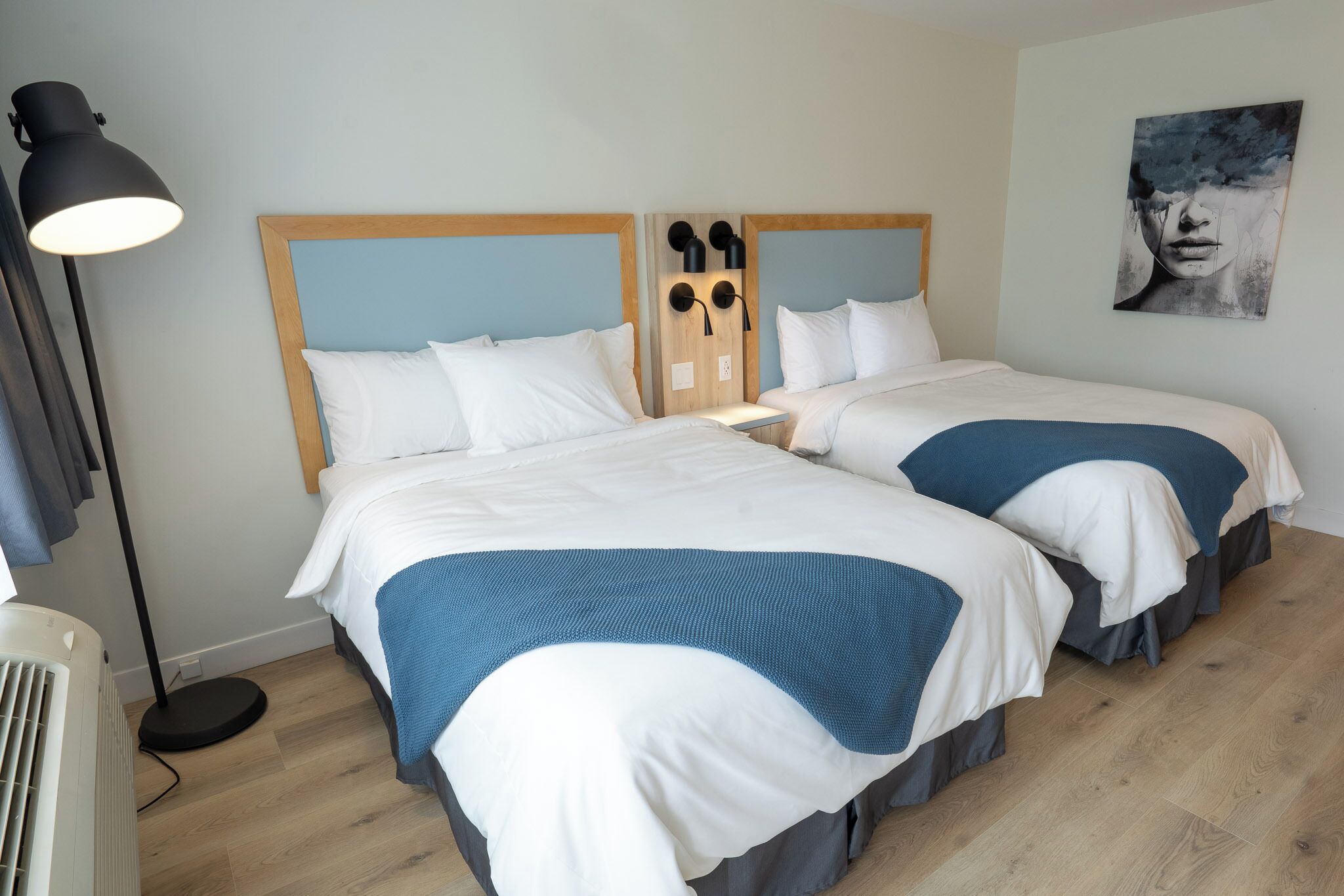 A hotel room with two beds, a floor lamp, and a wall-mounted light fixture.