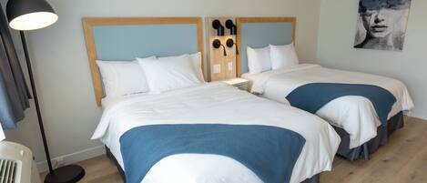 A hotel room with two beds, a floor lamp, and a wall-mounted light fixture.