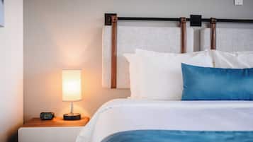 A neatly made bed with white and blue bedding, a bedside lamp, and a digital clock on a wooden nightstand.