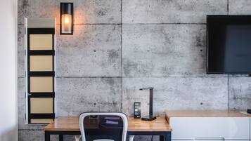 A modern room with a concrete wall, a wooden desk, a white chair, a black lamp, and a TV mounted on the wall.