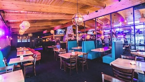 Een restaurant met houten balken in het plafond, tafels en blauwe zitjes.