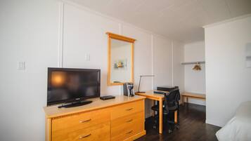 A hotel room with a wooden dresser, a flat-screen TV, a desk with a chair, and a bed.