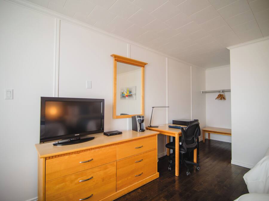 A hotel room with a wooden dresser, a flat-screen TV, a desk with a chair, and a bed.