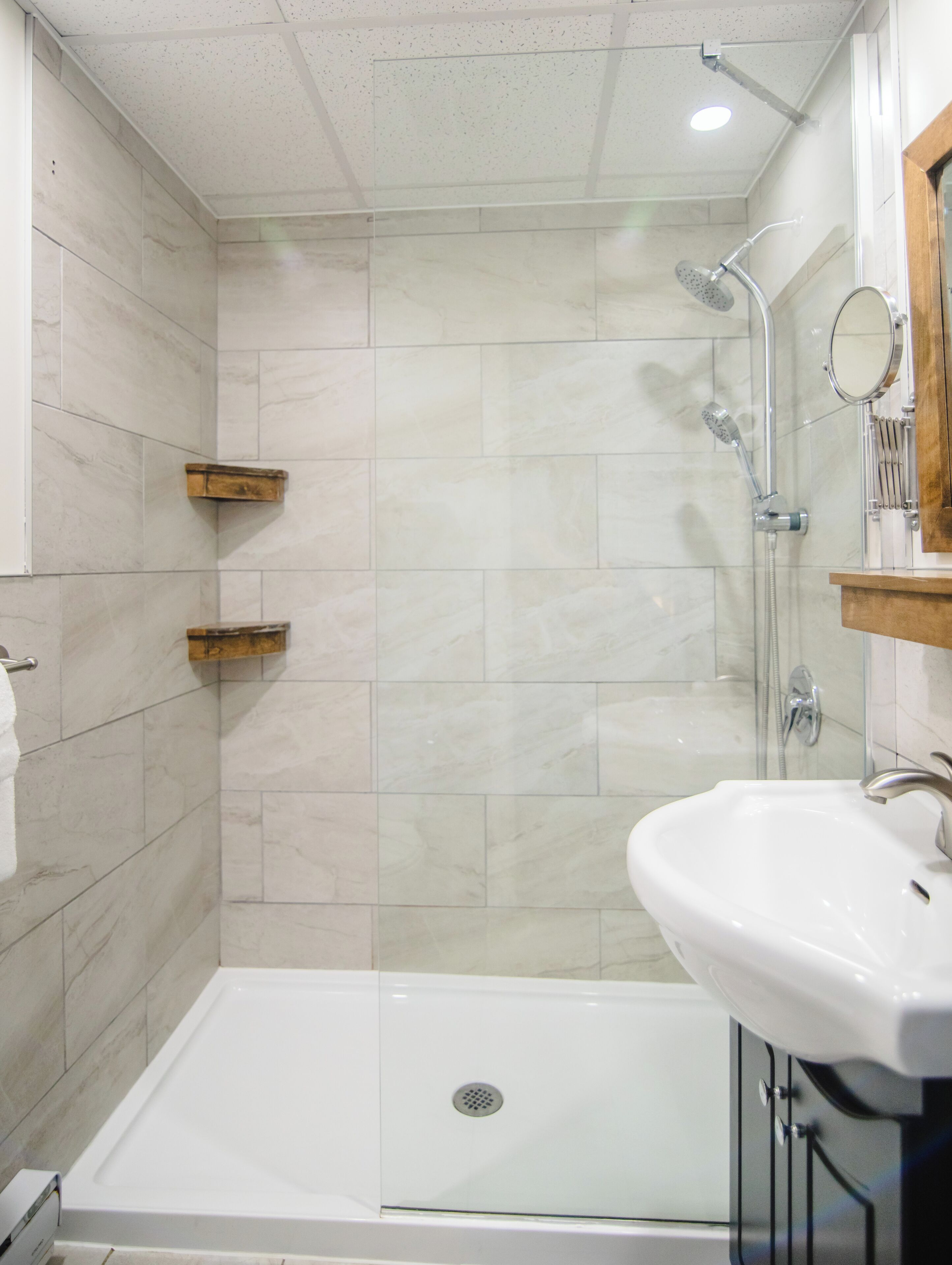 A modern bathroom with a glass shower enclosure, a white sink, and wooden shelves.