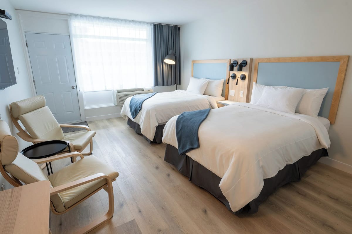 Habitación de hotel con dos camas, un escritorio, una silla y un ventanal con cortinas.