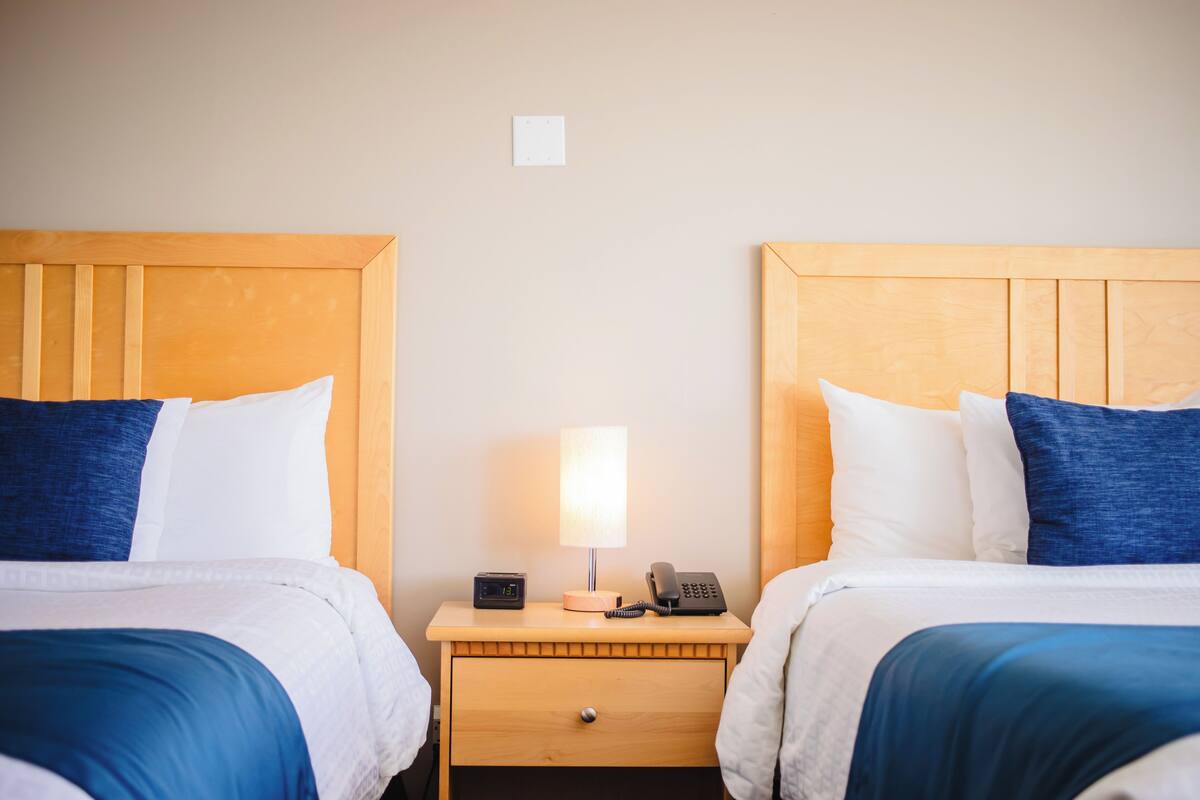Una habitación de hotel con dos camas, cada una con cabecero de madera, una mesita de noche entre ellas y una lámpara.