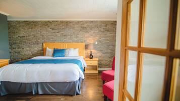 Een slaapkamer met een bakstenen muur, een houten hoofdbord, een bed met blauw beddengoed, een nachtkastje met een lamp en een rode stoel.