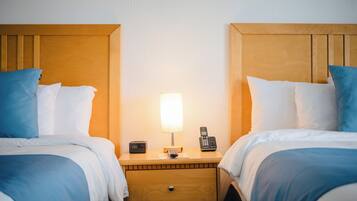 A hotel room with two beds, each with blue and white bedding, a wooden headboard, a bedside table with a lamp, a phone, and a small drawer.