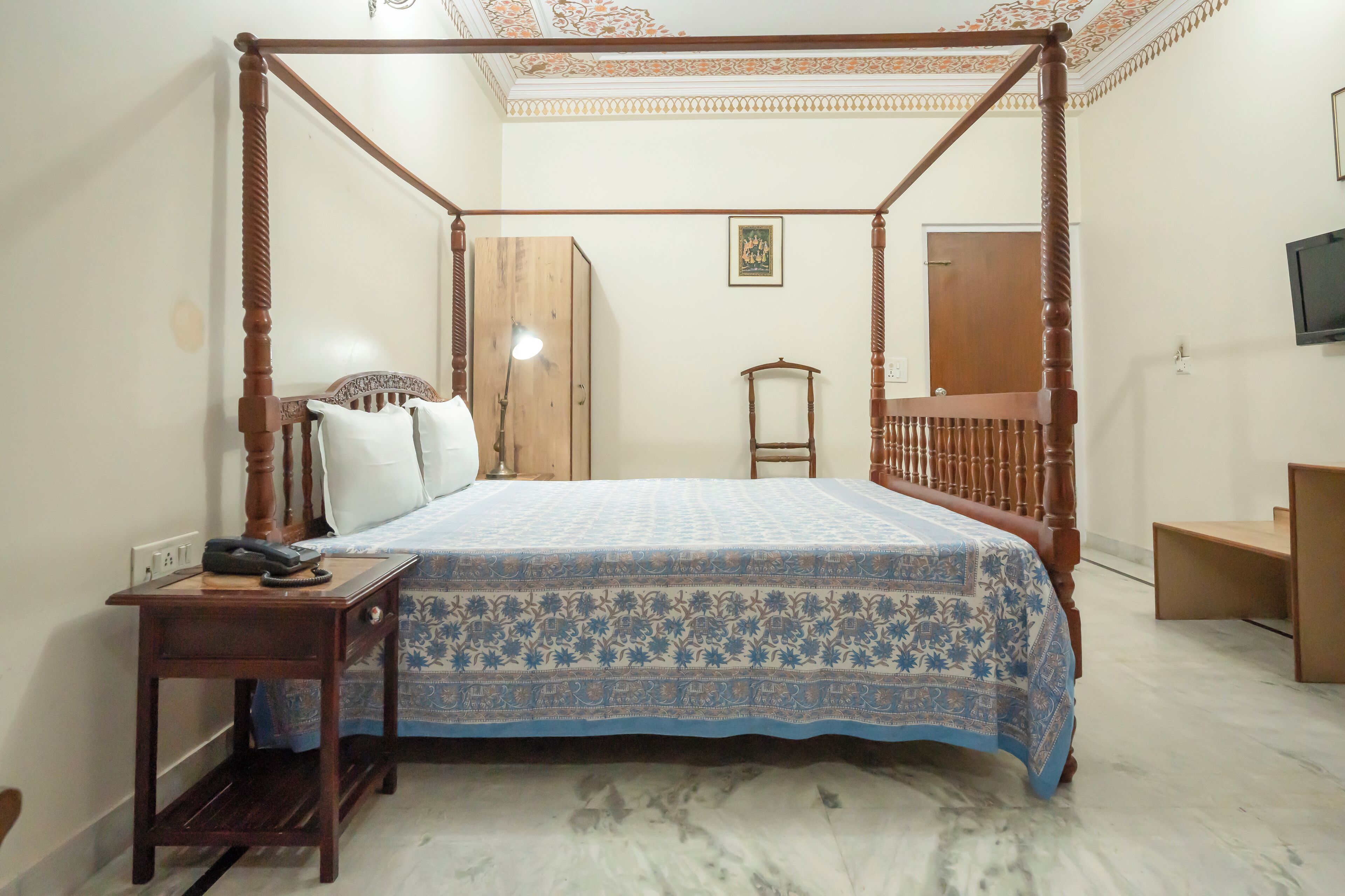 Una cama con dosel con una colcha estampada, una mesita de noche con lámpara y un armario de madera.