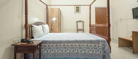 Una cama con dosel con una colcha estampada, una mesita de noche con lámpara y un armario de madera.