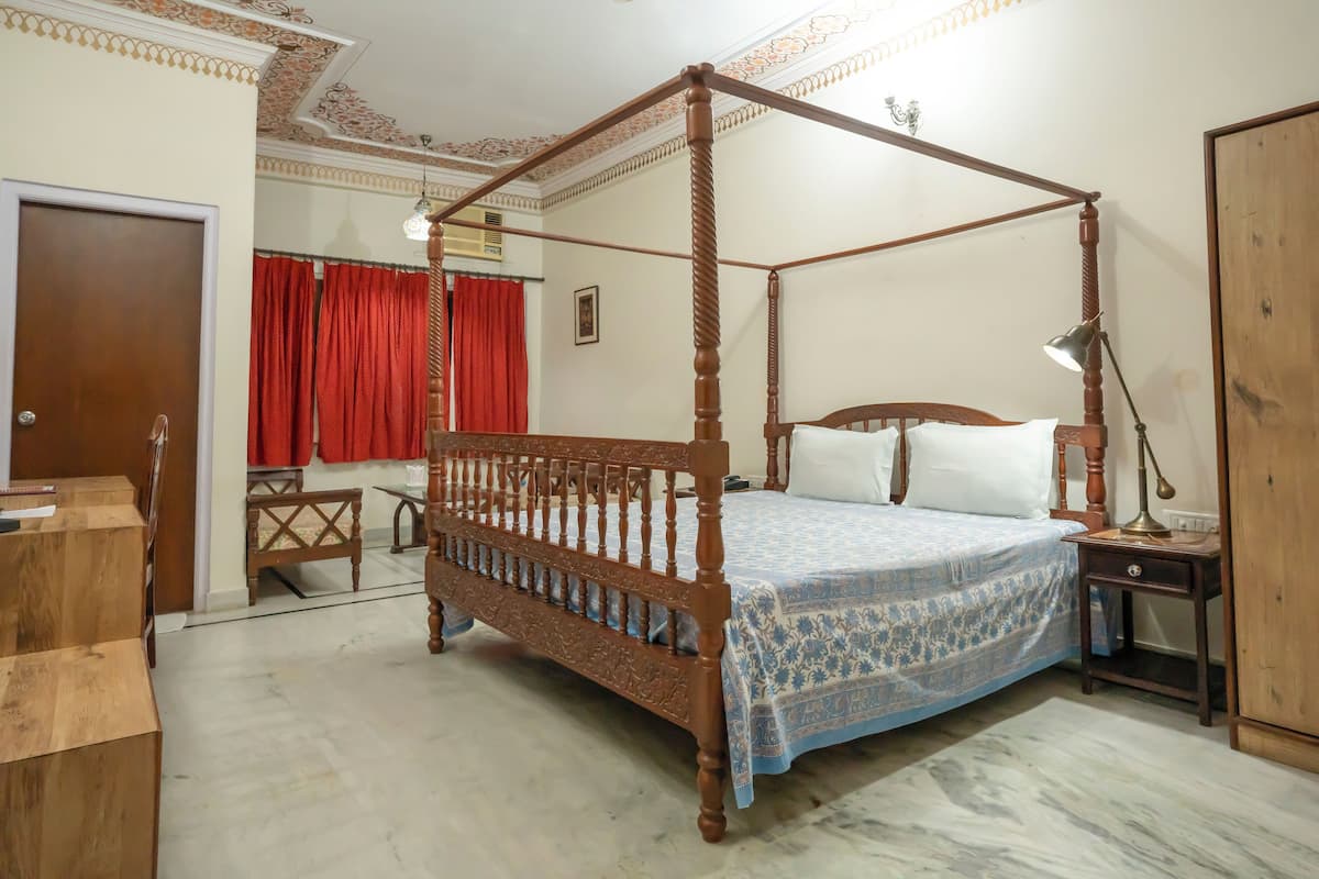 Una cama con dosel de madera y colcha estampada azul, una mesita de noche con lámpara y un armario de madera.