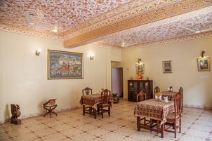 Uma área de refeições com teto estampado, uma pintura grande emoldurada e um armário com objetos decorativos.