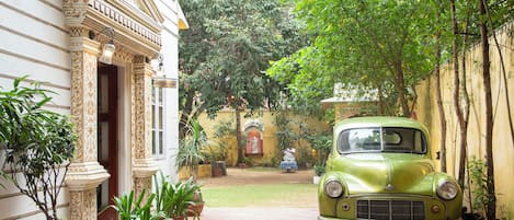 A vintage green car parked in a courtyard with ornate architecture and potted plants.