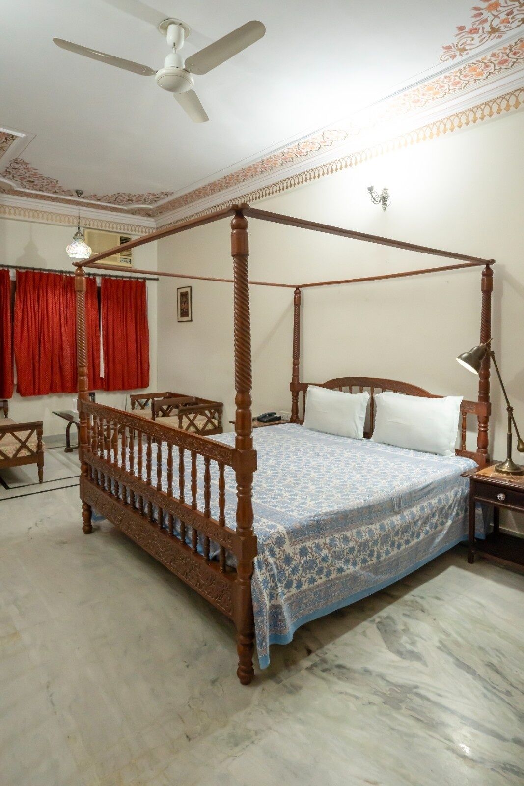 Uma cama de dossel com colcha estampada, um ventilador de teto e uma cortina vermelha.